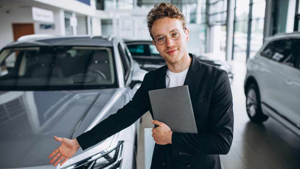 Ein Verkäufer zeigt auf ein Auto und erklärt dem Kunden die Konditionen beim Auto verkaufen Dortmund